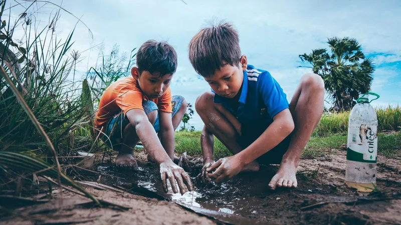 Two children playing with their hands in a stream at the edge of a field